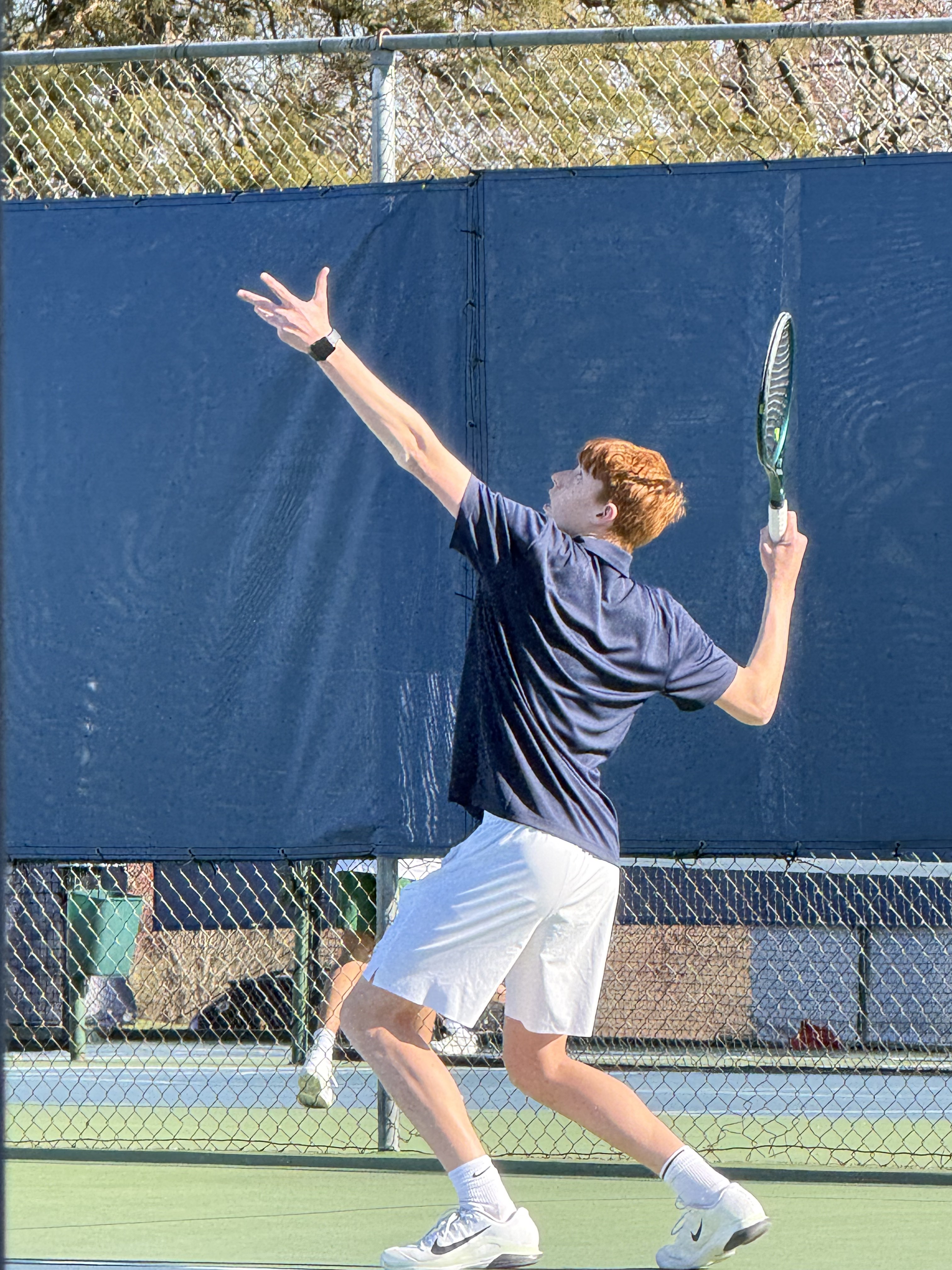 Coach reaching up mid-serve on a hard court